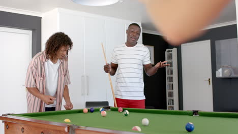 un joven afroamericano y un hombre biracial disfrutan de un juego de billar en casa.