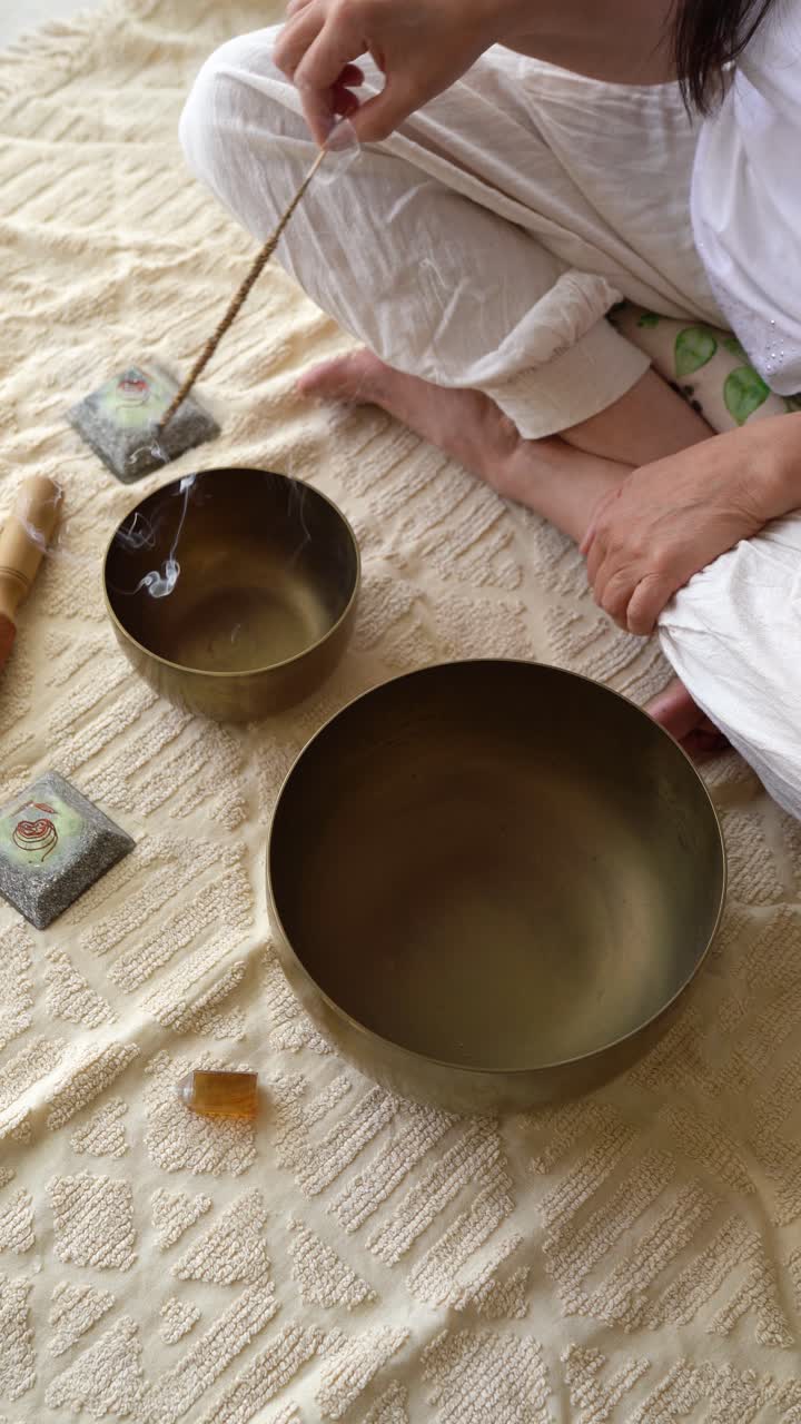 Person Sitting Cross-legged With Tibetan Singing Bowls, Incense, And Crystals On A Mat. Meditation Concept. vertical shot