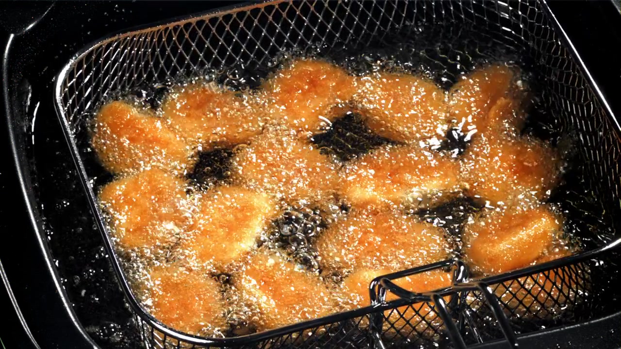 熱い油の中で揚げられているきつね色のチキンナゲット。