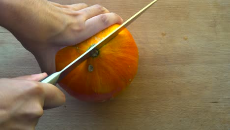 top down view of male hands struggling to cut a hokkaido pumpkin in half