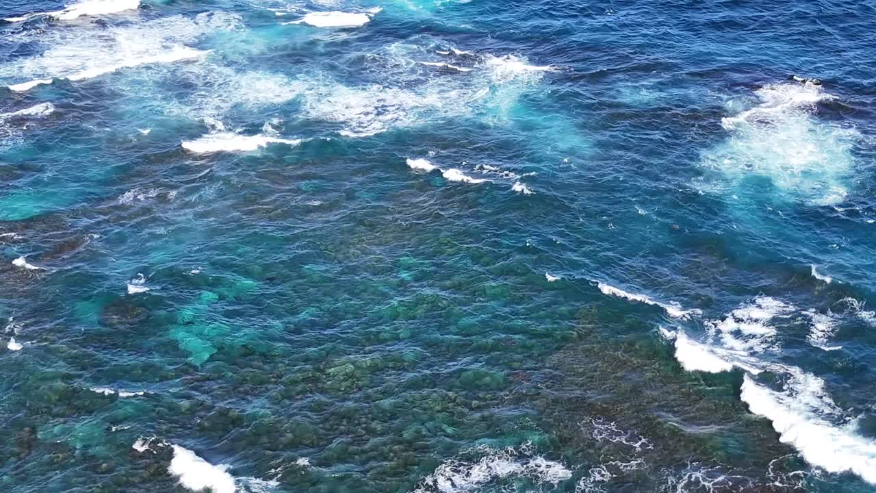 Vibrant turquoise waters with white foam create dynamic patterns over submerged rocks.