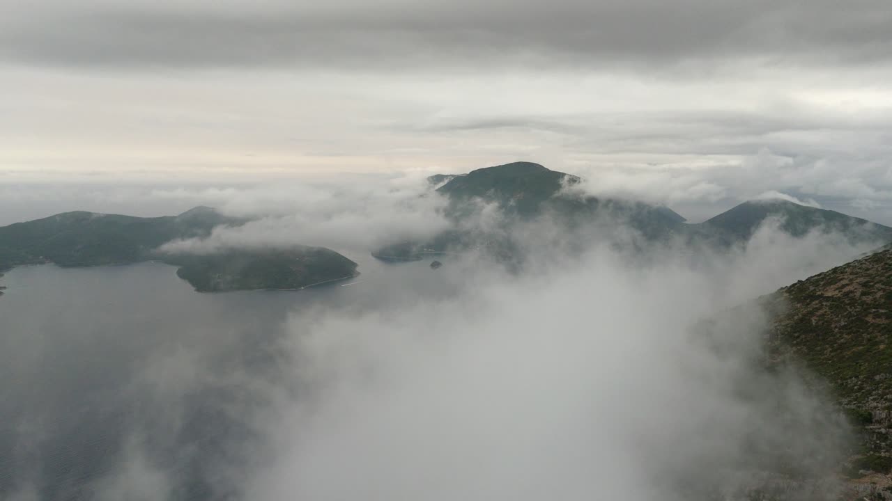 Aerial drone view through low-hanging clouds and fog over scenic Ithaca Island, Greece. A moody and atmospheric landscape on an overcast day in Europe.