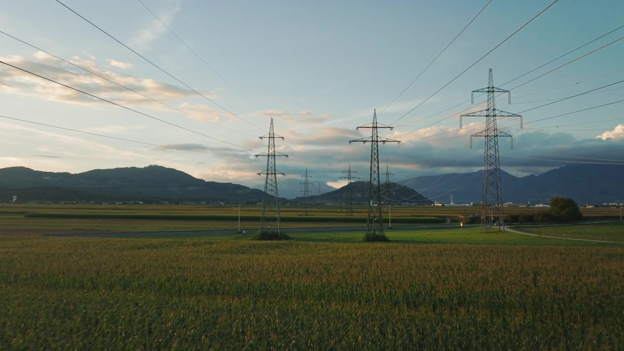 Power lines and electric towers connect across a rural area during sunset