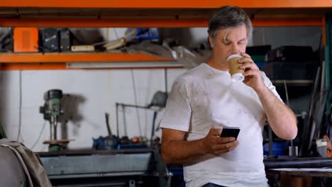 Männlicher-Mechaniker-Trinkt-Kaffee,-Während-Er-Das-Mobiltelefon-4k-Benutzt