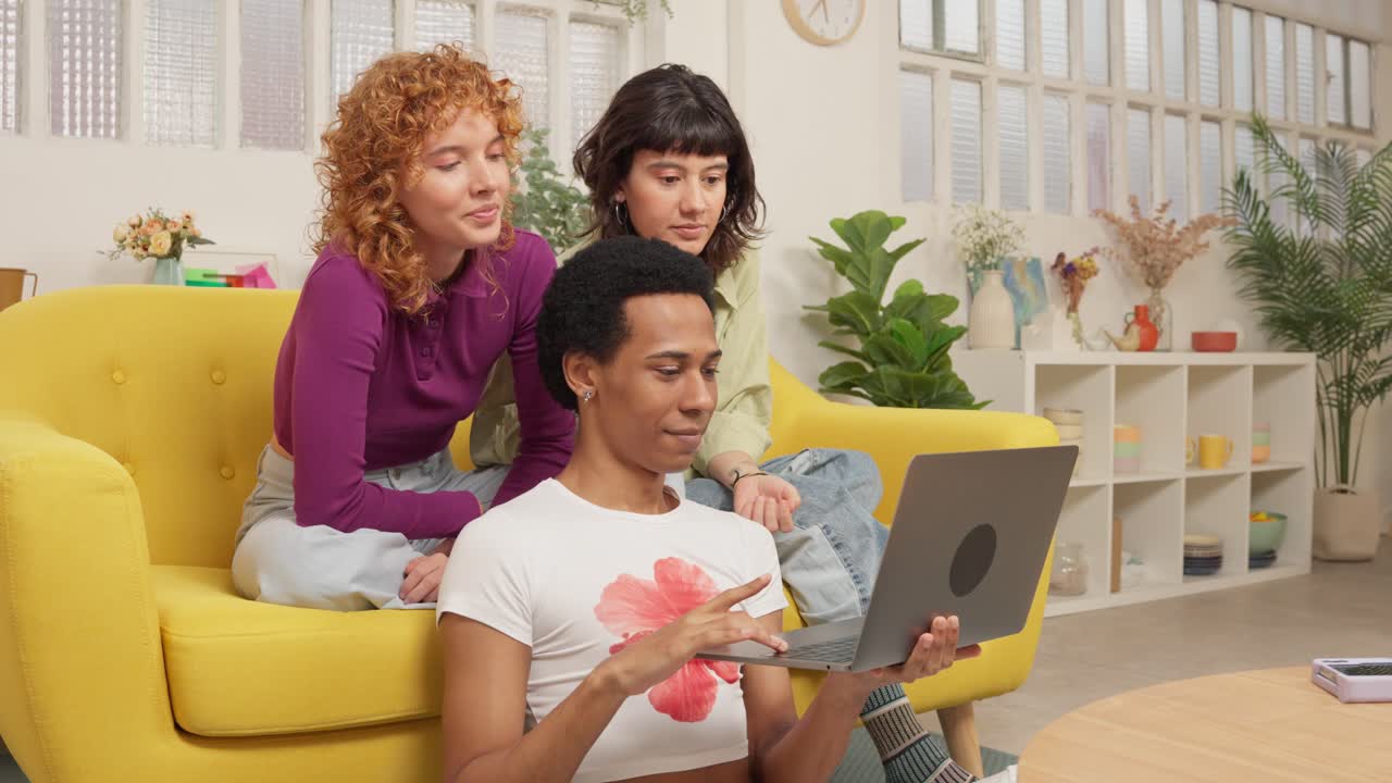 Three friends using a laptop on a yellow couch