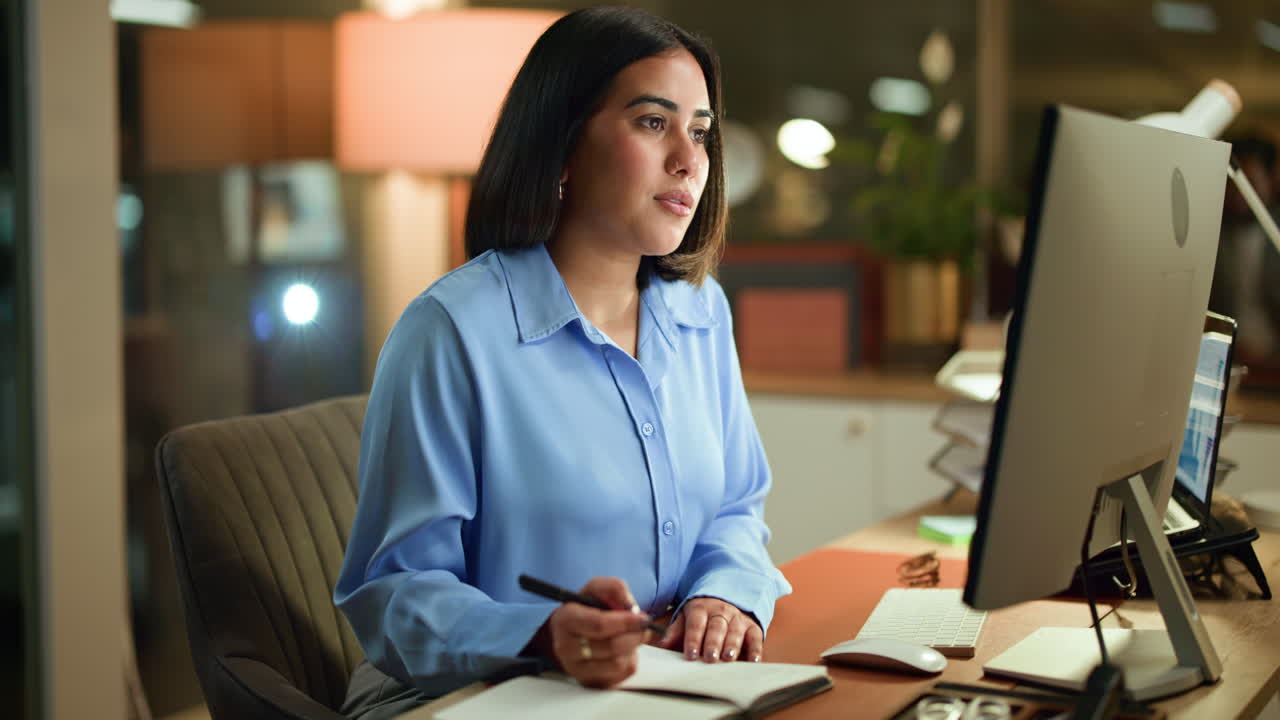 Woman working at desk with computer and notebook