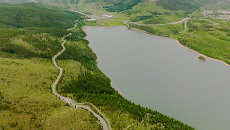Beautiful lake locating in the mountainous territory and surrounded by greenery. Wavy road for transport going along the waterfront. Aerial view.