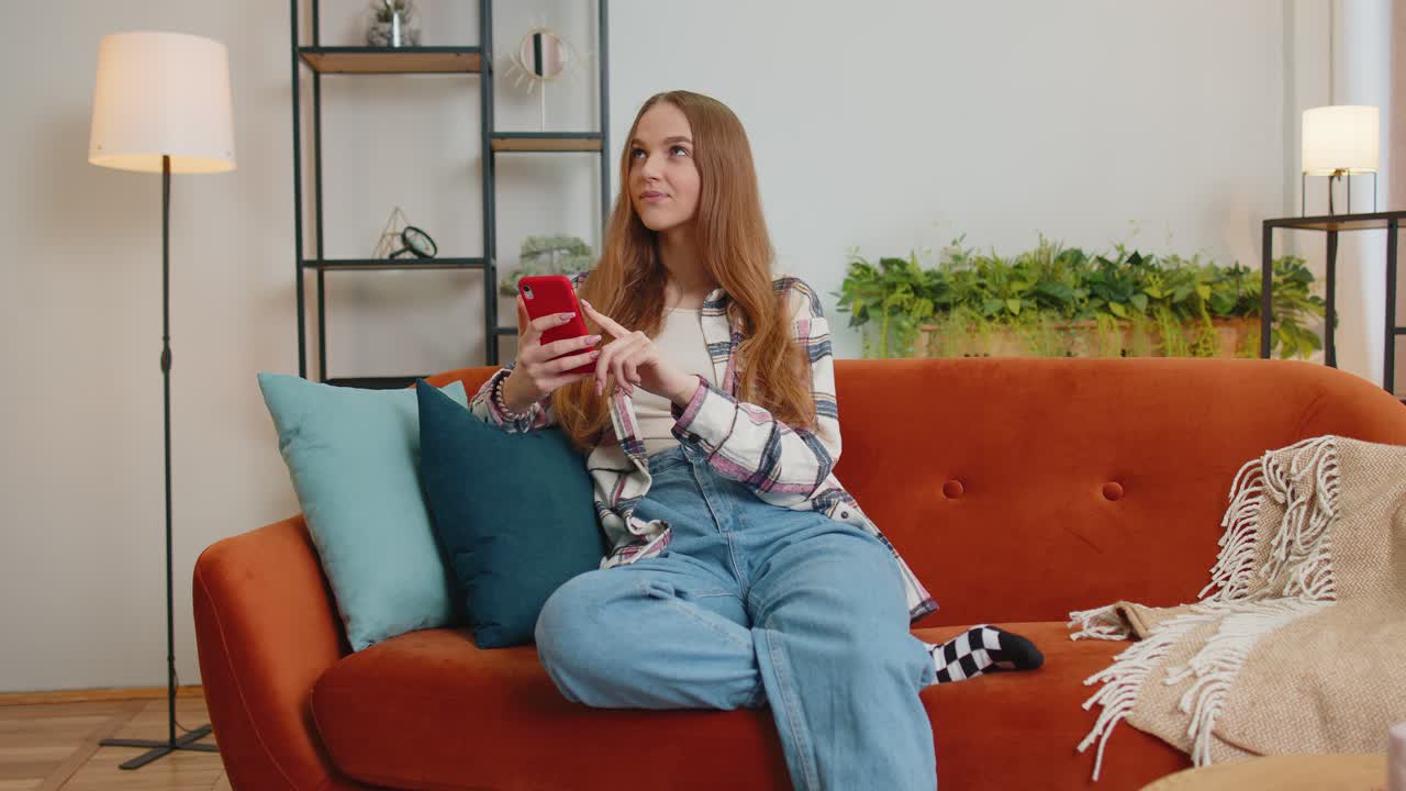 Cheerful young woman sitting on sofa using mobile phone share messages on social media application