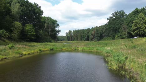 "Drone-soars-over-Europe's-dawn-lit-lake,-revealing-tranquil-lagoon,-lush-forest,-and-natural-ponds