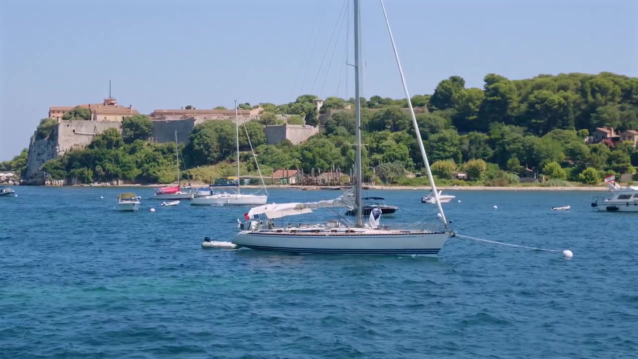 Ampia vista di una storica fortezza in cima a una scogliera con una barca a vela bianca ancorata nelle acque calme sottostanti, Isola di Santa Margherita, Francia.