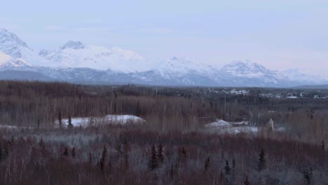 anchorage, pan over forest in winter with snow capped mountains in alaska