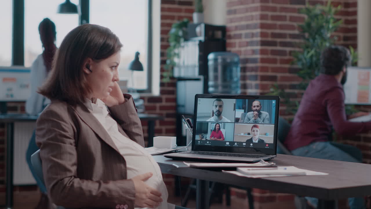 Pregnant employee using business video call on laptop to talk to workmates