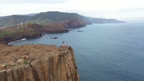 drone shot of a woman walking on the edge of a cliff in a dress in the wind in madeira