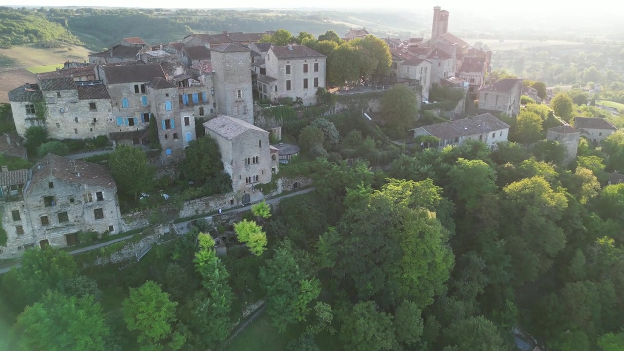 Vista aerea con drone nella campagna francese di una piccola e antica città medievale in mattoni sulla cima di una montagna, circondata da campi verdi, in avvicinamento in una giornata di sole a Cordes-sur-Ciel