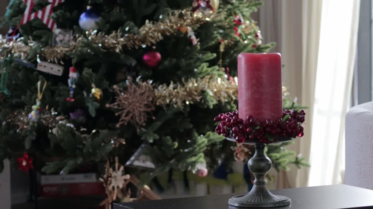 A hand reaches into frame with a lighter to light a decorative Christmas candle in front of a Christmas tree
