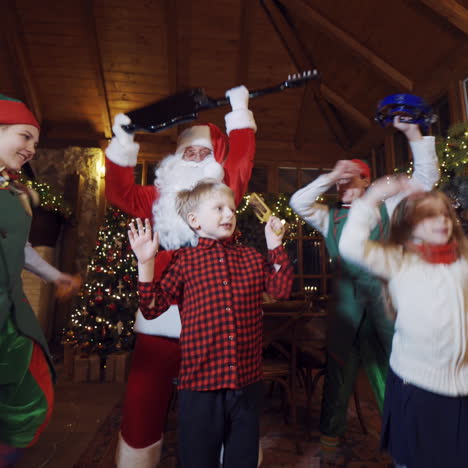 funny santa with guitar, elves and kids dancing happily together at christmas. joyful celebration christmas inside the decorated house.