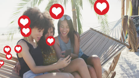 Animación-De-Iconos-Digitales-De-Amor-De-Corazón-Rojo-Sobre-Amigas-En-Hamaca-Con-Teléfono-Inteligente-En-La-Playa