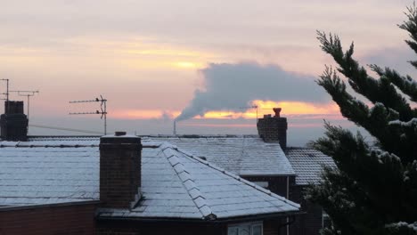 smoking industry chimney above frosty white winter home rooftops glowing sunrise orange sky