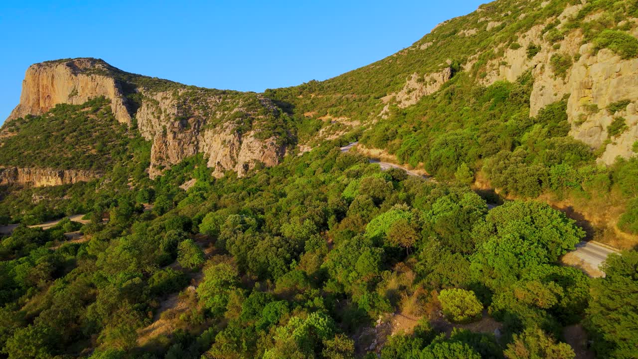 A mountain side with lots of green trees and a red colored cliff face. Location: Tunisia, Zaghouan , Sidi Bougabrine.