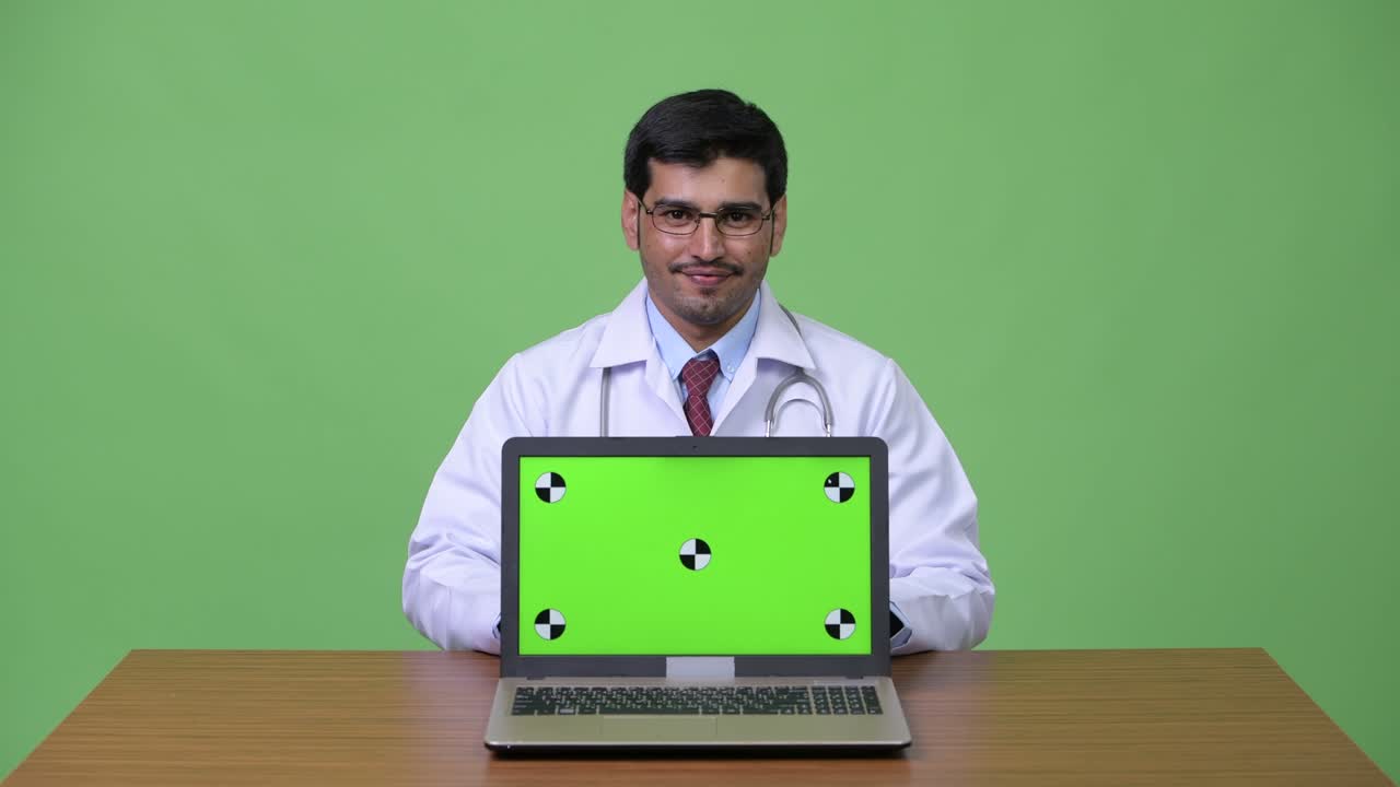 Young handsome Persian man doctor showing laptop
