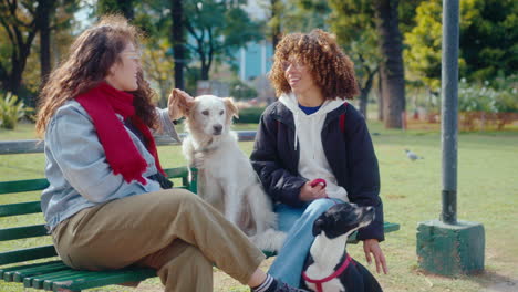 women sitting on bench in the park, petting dogs and talking