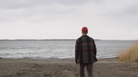 rear view of a teenage boy dressed in an orange beanie and a plaid coat approaching the seashore