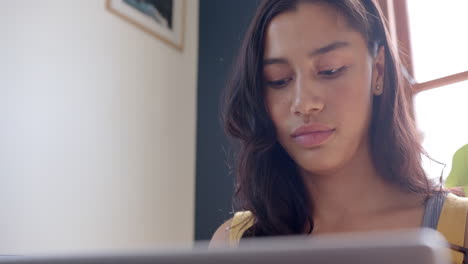 Focused-biracial-teenage-girl-sitting-on-couch-using-laptop,-slow-motion