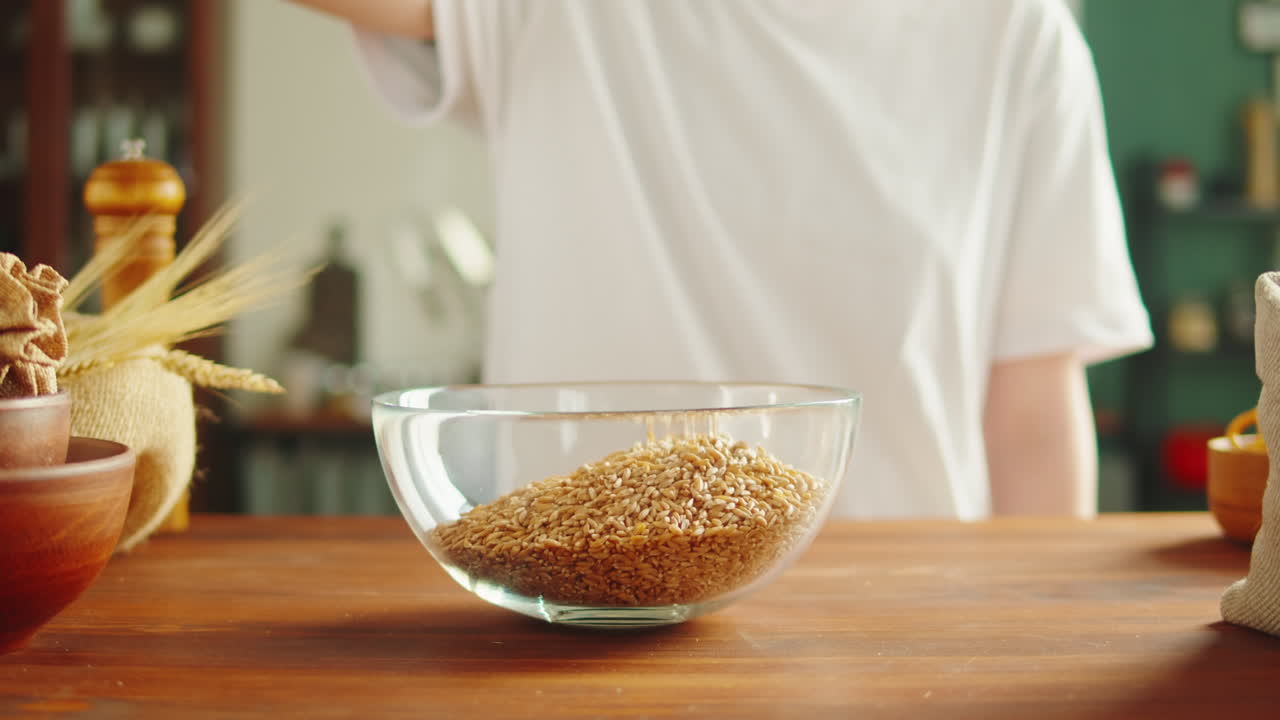 Person Pouring Grain from a Jar into a Glass Bowl in a Kitchen