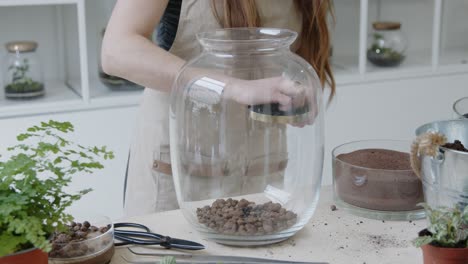 a young woman prepares a glass terrarium for creating the small live plant ecosystem in it - a forest-in-a-jar concept close-up