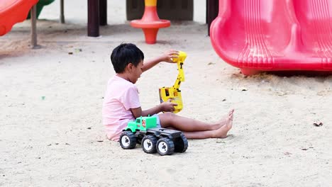 young boy enjoys playing with toy vehicles in sand