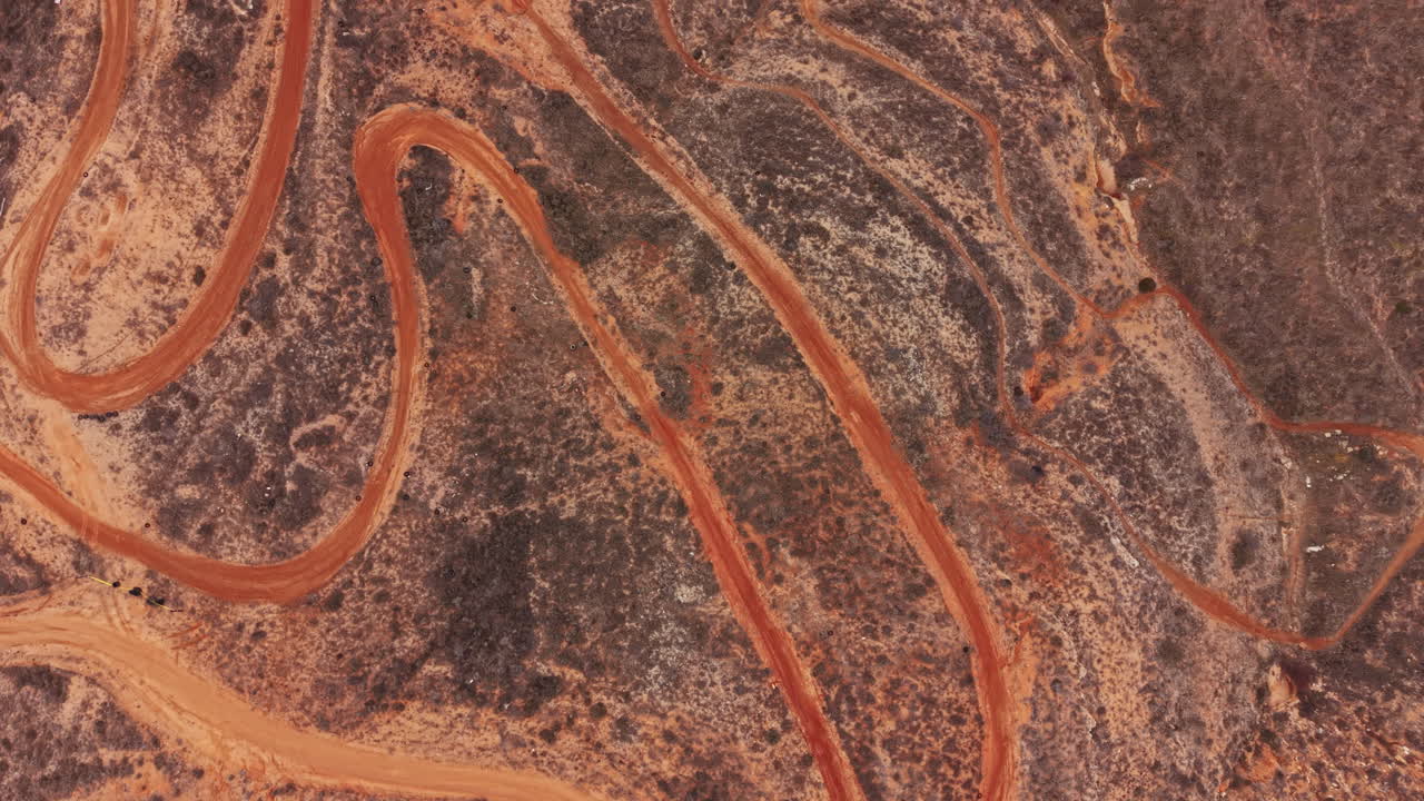 Una tortuosa strada sterrata attraversa un paesaggio arido in una zona remota dell'Australia, durante il giorno.