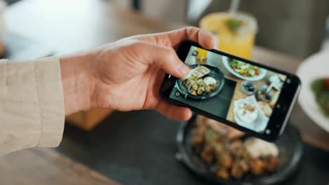 primer plano de la mano masculina tomando una foto en la comida del teléfono inteligente en la mesa