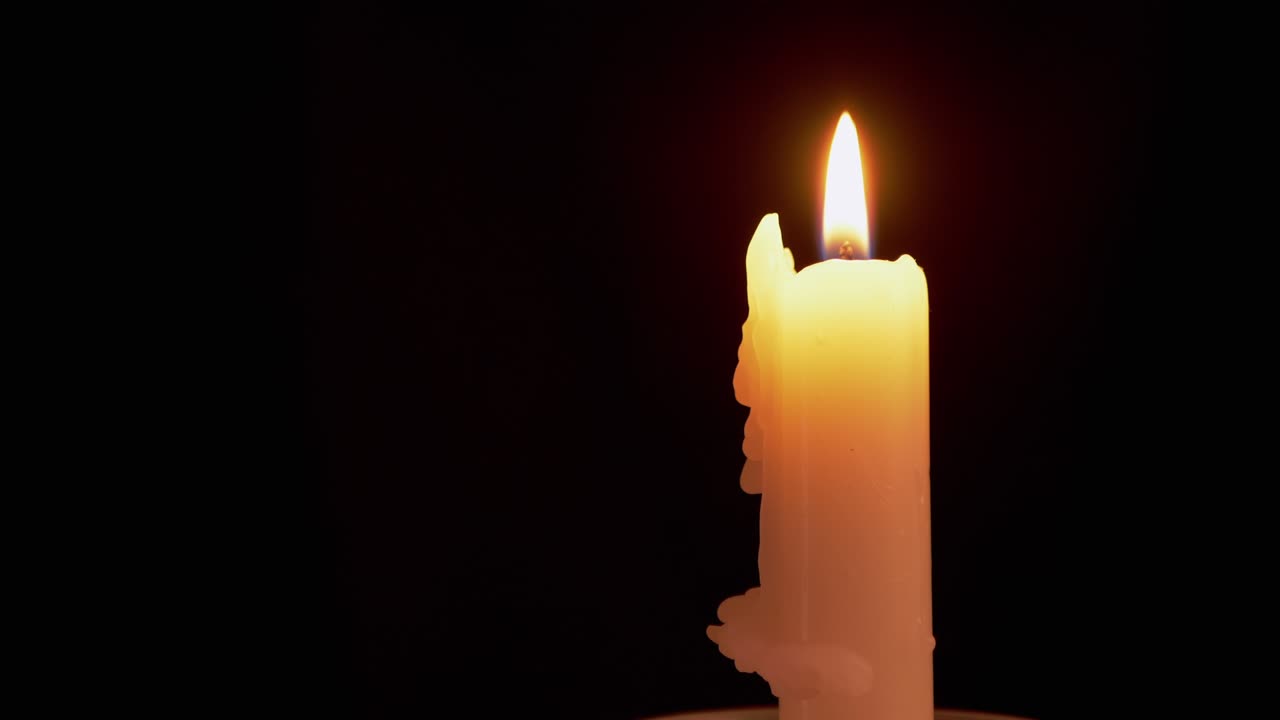 Candela di paraffina gialla che brucia con una fiamma calma e uniforme su sfondo nero.