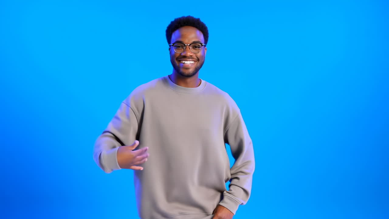 Smiling Black Man Blue Background Hosting, Wearing Gray Sweater And Glasses, Making Playful Arm Gestures