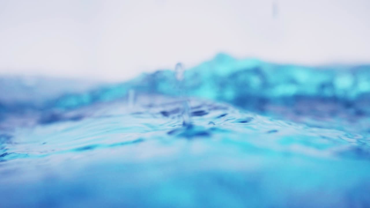 슬로우 모션의 깨끗한 물 표면은 물이 튀는 상점으로 화면을 채우고 기포로 액체 표면을 흔들고 있습니다.