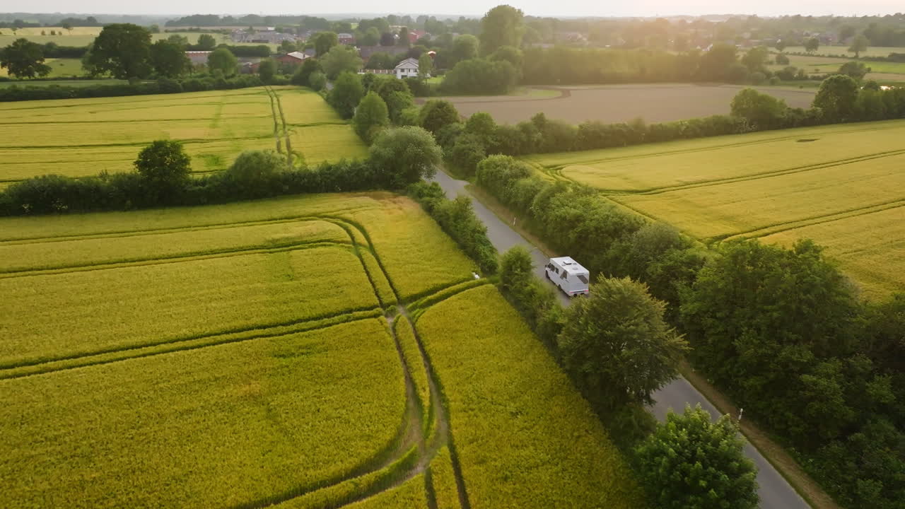 Aerial view following a RV driving in middle of blooming canola fields, sunset