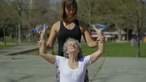 concentrated senior woman doing exercises with trainer in park.