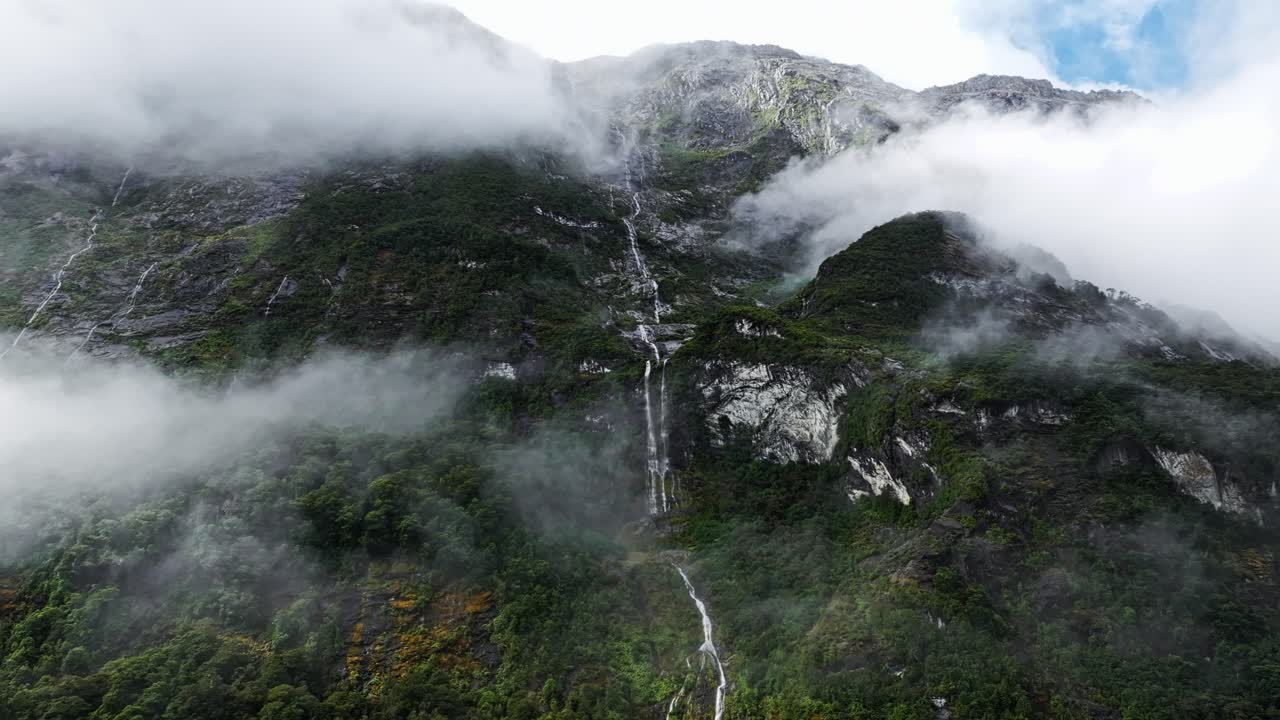 una increíble cascada delgada desciende en cascada entre las nubes y el bosque en milford sound, paralaje aéreo