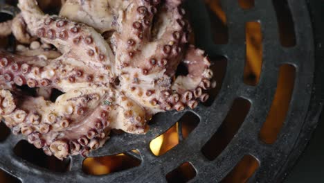 top-down handheld close-up shot van malse gerookte octopus die wordt gekookt op een barbecueroker met zichtbare vlam aan de onderkant