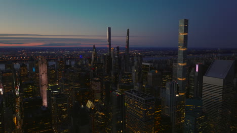 Ascending-shot-of-evening-downtown.-Modern-high-rise-buildings-with-lighted-windows-and-colourful-sky-after-sunset.-Manhattan,-New-York-City,-USA