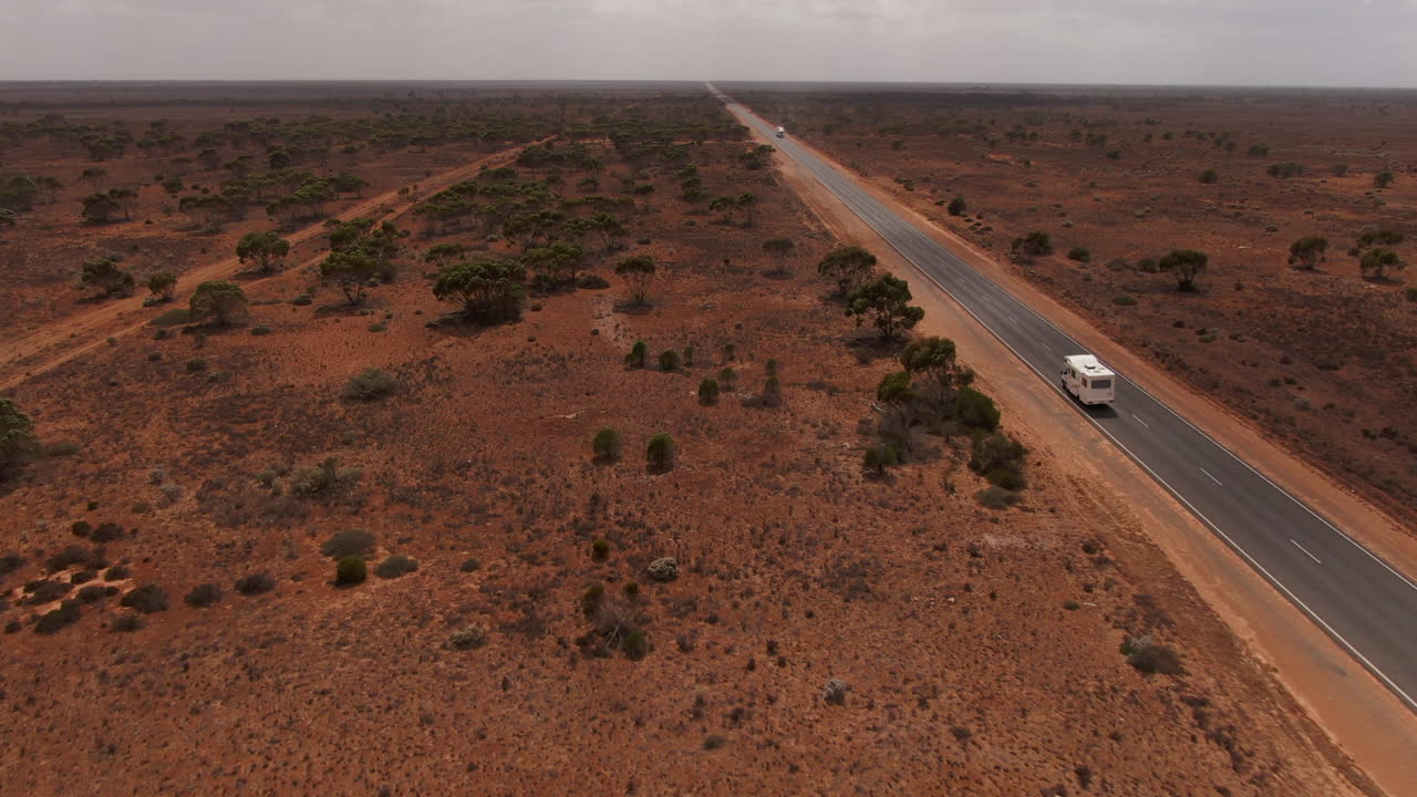 흐린 날 붉은 사막으로 둘러싸인 호주의 빈 도로에서 캠퍼 밴의 공중 전망