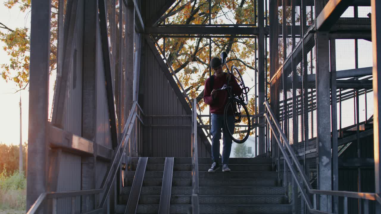 hombre llevando una bicicleta por las escaleras metálicas al atardecer