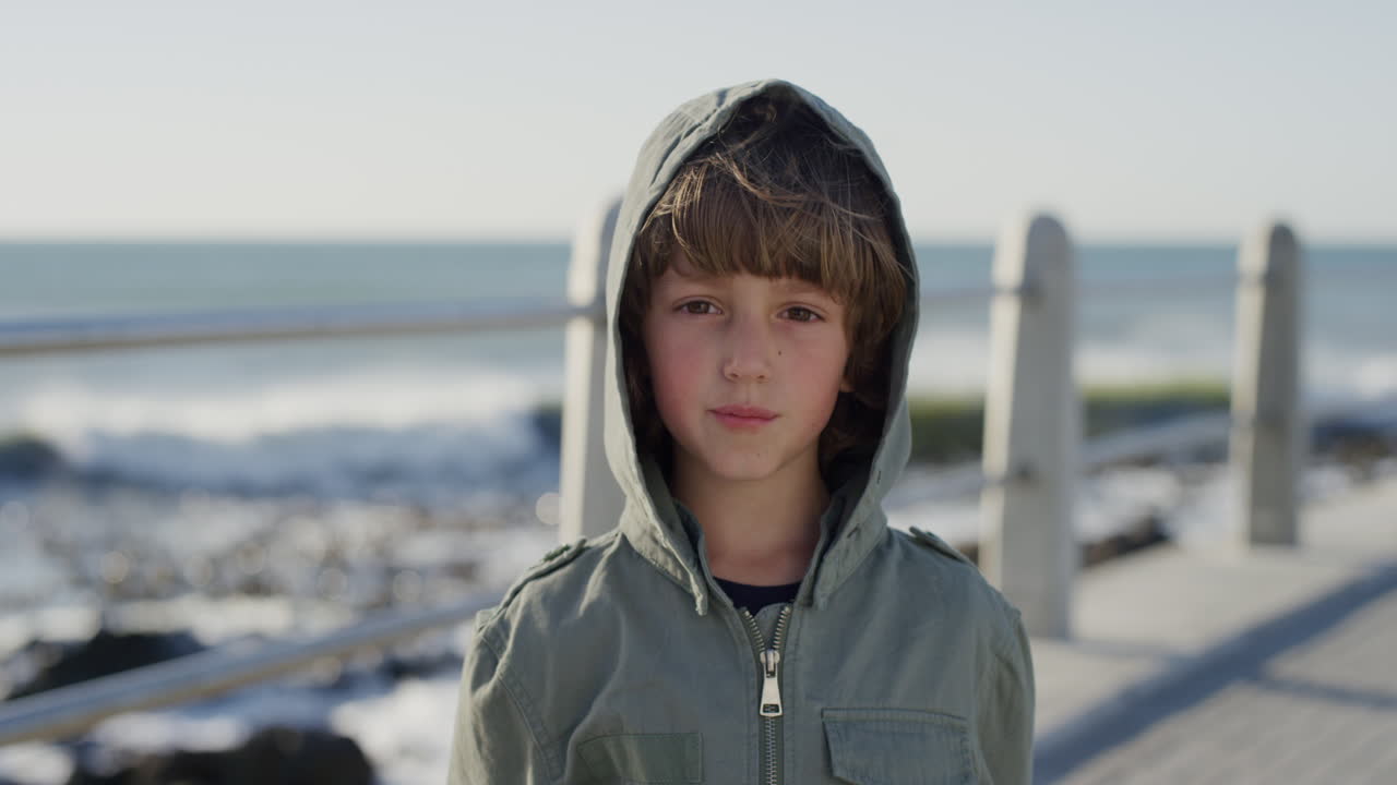 retrato de un niño caucásico feliz disfrutando de la playa del océano con chaqueta en un día soleado y ventoso en cámara lenta