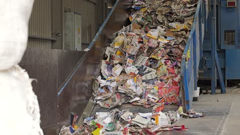 una gran garra de tractor agrega residuos de papel a la cinta transportadora en la planta de reciclaje de papel