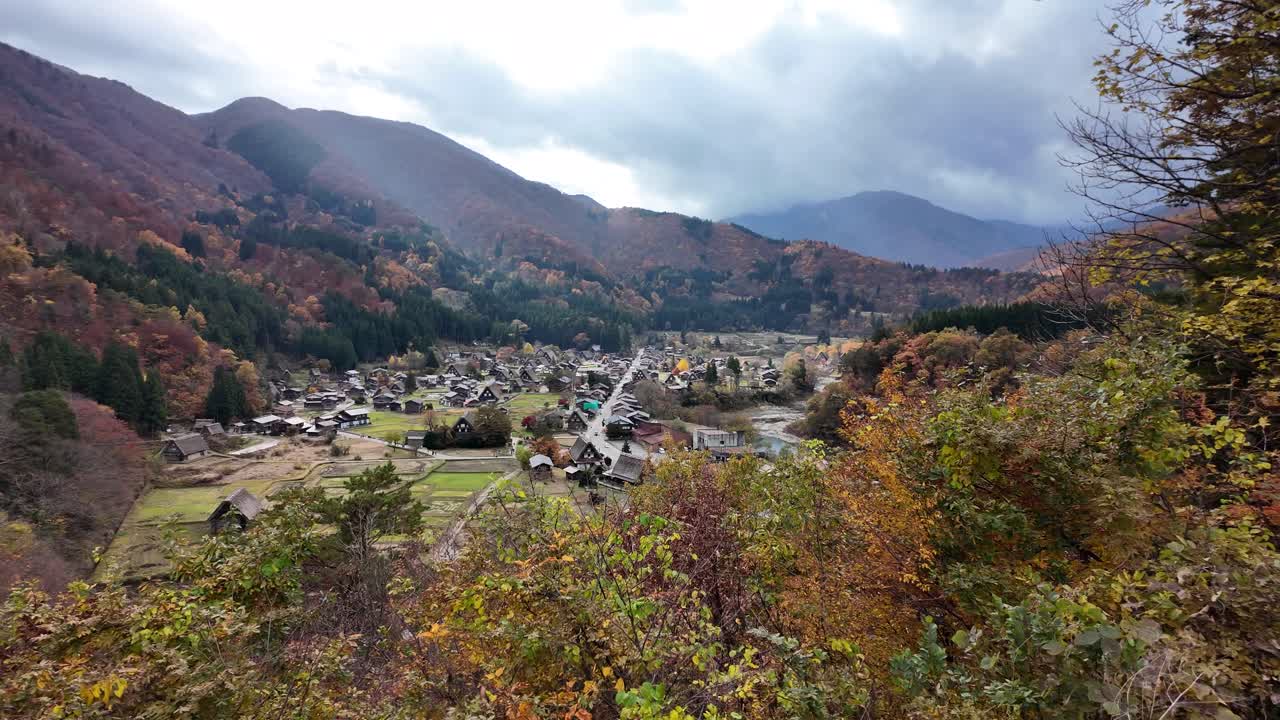 Shirakawa-go village's traditional houses nestled in a valley surrounded by vibrant autumn foliage.