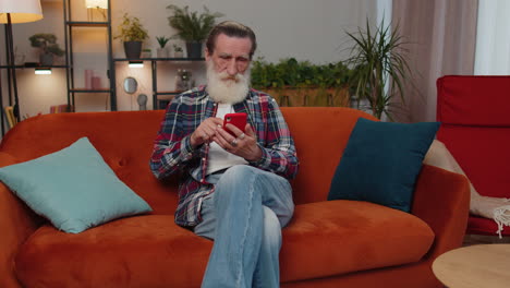 senior old grandfather sitting on sofa, using smartphone share messages on social media application