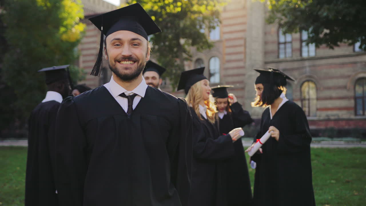Portrait of a young graduate in black traditional gown and cap posing to the camera and celebrating