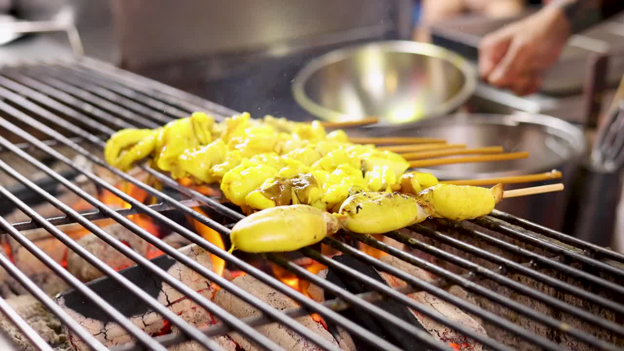 Vendor grills yellow squid roe skewers over open flame, vibrant street food scene, shallow focus