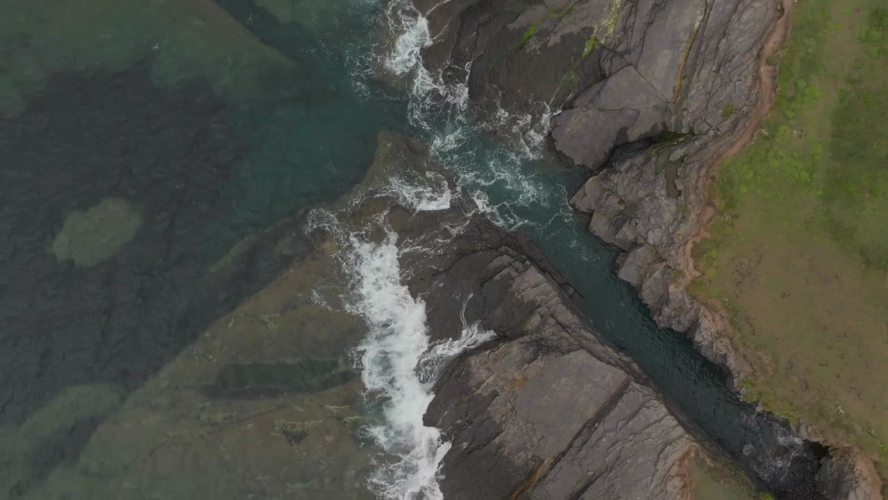 Una ripresa aerea minimalista dall'alto di onde che si infrangono contro rocce scure sulla costa irlandese, che mostra l'autentica bellezza naturale e la sostenibilità.