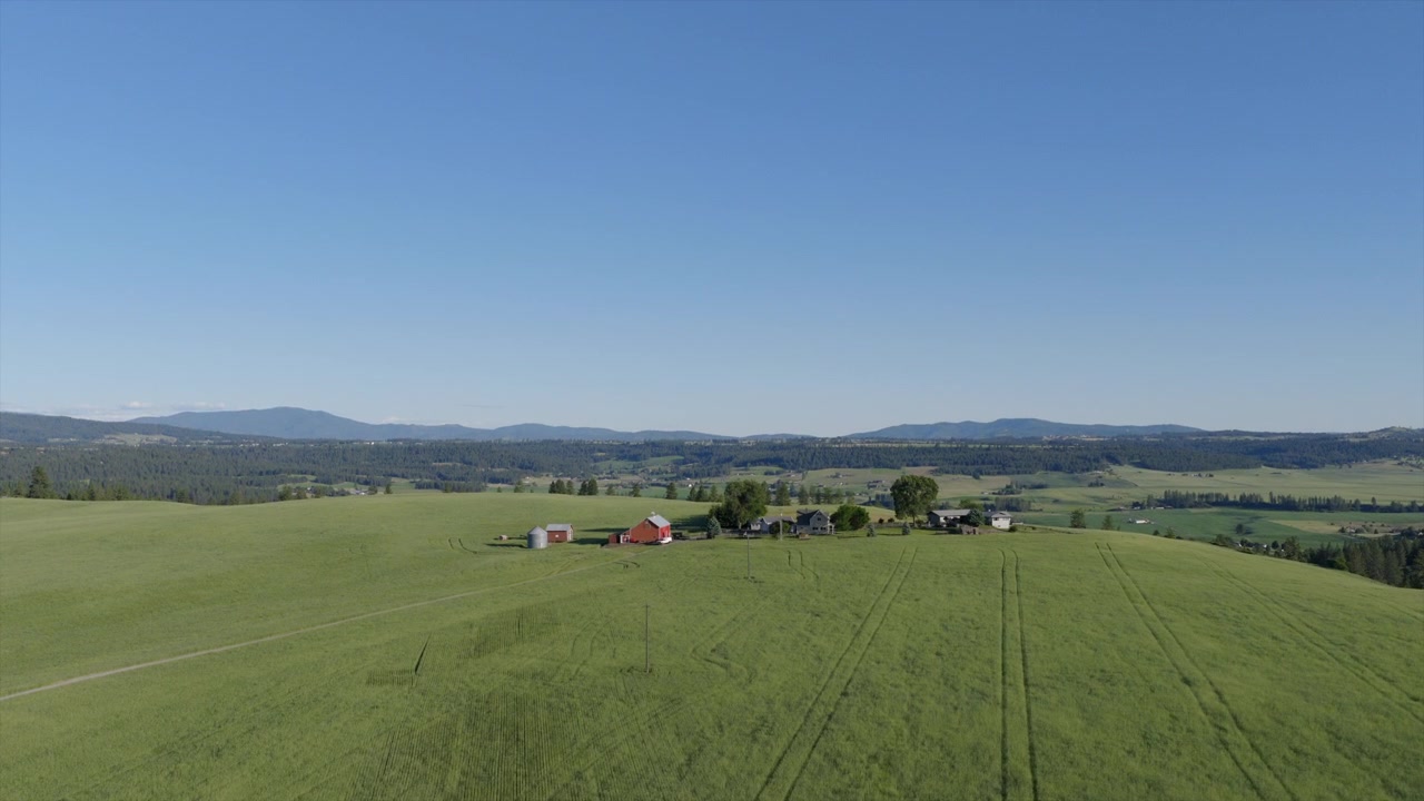 Breed luchtbeeld van een boerderij en bijgebouwen te midden van groene velden, met bergen die zich uitstrekken langs de horizon van Spokane, WA